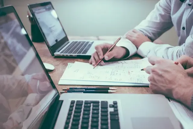 Dvoje ljudi radi na laptopima i bilježi financijske podatke